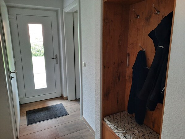 A hallway with a wooden bench, a coat rack, and a door leading to a bright room.