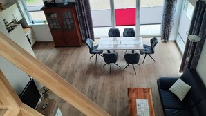 A dining area with a table and chairs, a wooden cabinet, and a view of the outdoors through large windows. - Ankerplatz in Idyllischer Umgebung und Nähe zum Bernsteinsee (Wiefelstede)
