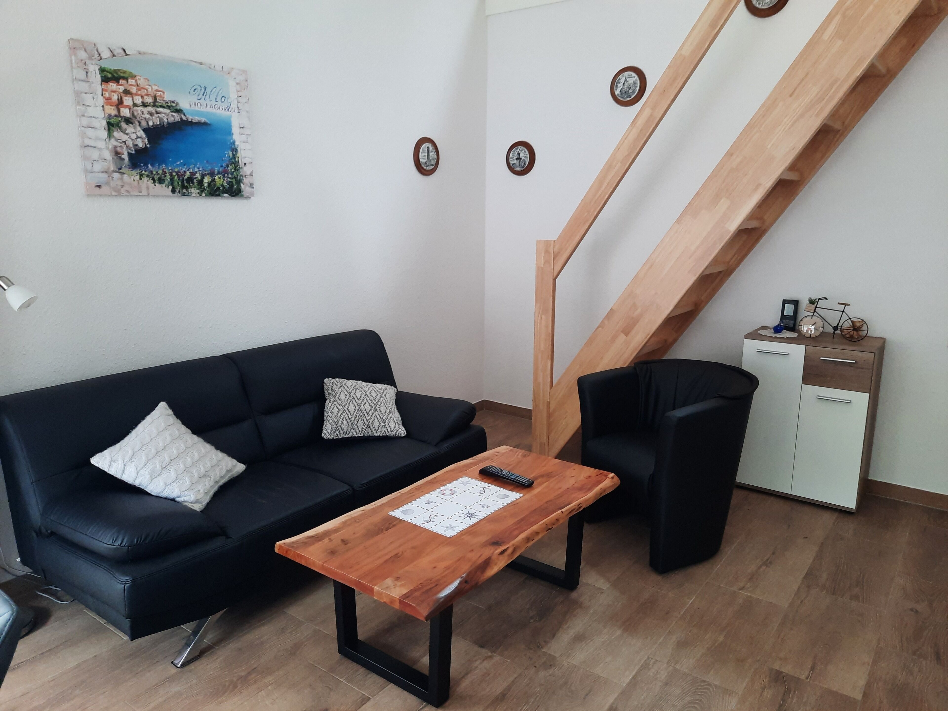 A living room with a black sofa, a wooden coffee table, a staircase, and a small cabinet with a bicycle on top.