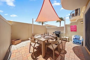 Un patio con tavolo apparecchiato per mangiare, un barbecue e una zona ombreggiata.