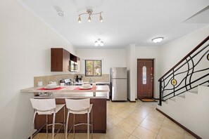 Eine moderne Küche mit einer zentralen Kochinsel, Barhocker, Edelstahlgeräten und einer Treppe mit dekorativer Geländer.