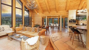 Un intérieur spacieux de chalet en bois, comprenant une grande salle à manger, une cuisine et un salon avec vue sur les montagnes.