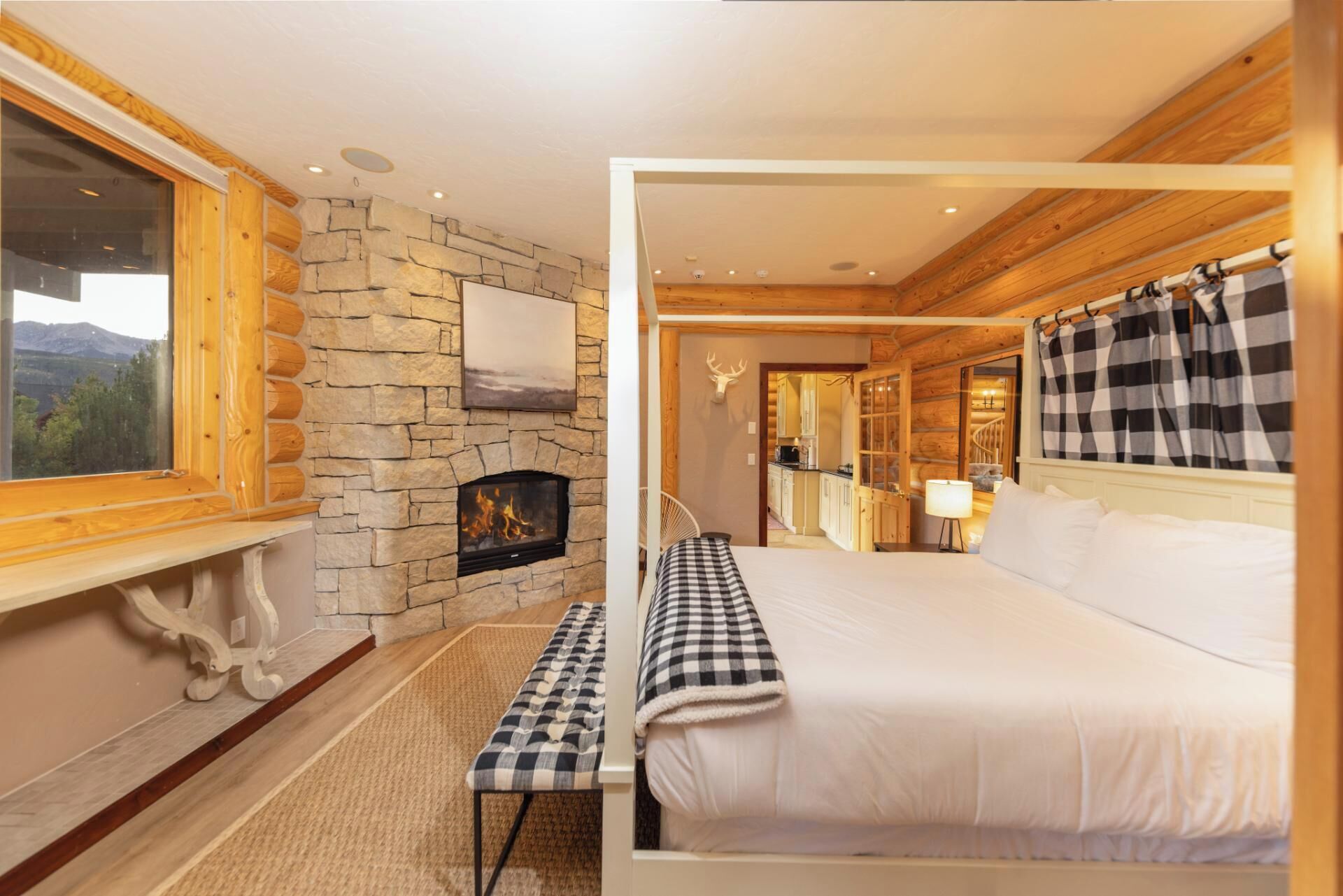A cozy room with a stone fireplace, a bed with checkered bedding, and a view of the mountains through a window.