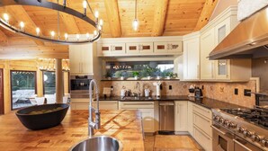 Une cuisine moderne avec un plancher en bois, un évier en acier inoxydable, une cuisinière à gaz et un grand îlot central sur lequel se trouve un panier de fruits.