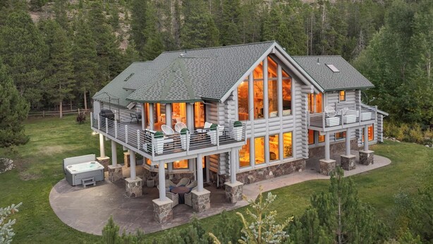 Une cabane en rondins dotée d’une grande terrasse, de piliers en pierre et d’un jacuzzi.