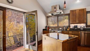 A modern kitchen with wooden cabinets, a large island, and a view of autumn trees through the sliding glass door. - Potato Patch Luxury 4 Bedroom Townhome - Vail Point (Vail)