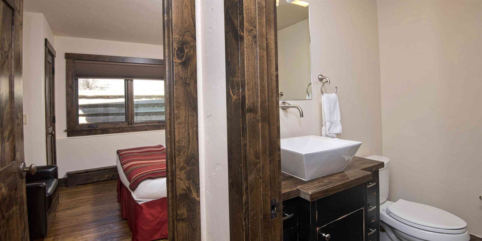 A bathroom with a wooden vanity, a white sink, a mirror, and a toilet.
