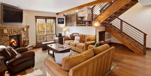 A living room with a fireplace, leather sofas, a coffee table, a TV, and a wooden staircase. - Potato Patch Luxury 4 Bedroom Townhome - Vail Point (Vail)