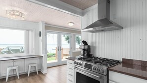 Ett modernt kök med vita skåp, en spis i rostfritt stål och ett stort fönster med utsikt över en uteplats.