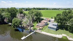 En fastighet vid en sjö med en brygga, ett hus och en stor grön äng i bakgrunden.