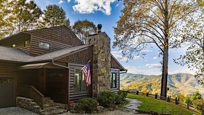 Une cabane en rondins avec une cheminée en pierre, un drapeau et un escalier en pierre menant à l’entrée.
