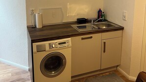 Une cuisine compacte équipée d’un lave-linge, d’un évier et d’un four à micro-ondes.
