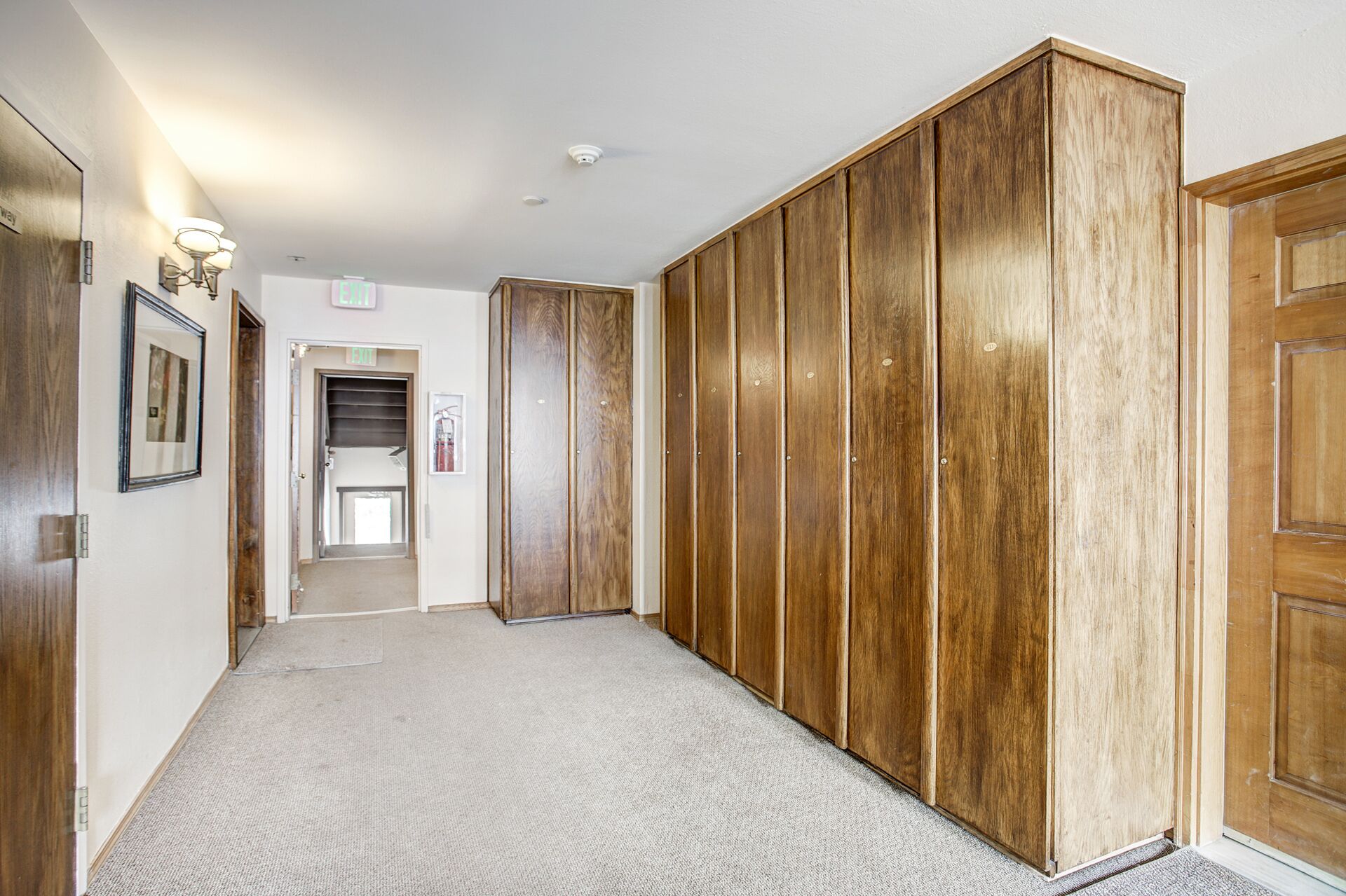Un couloir avec des portes en bois, un sol recouvert de moquette et un panneau indiquant la sortie.