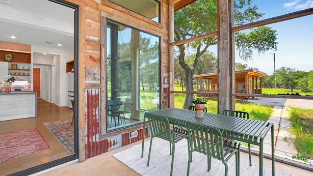 A modern house with large windows, a dining area with green metal chairs, and a view of the outdoors. - Wild Candy Farm - Breezeway Haus (Wimberley)