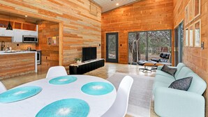 Un intérieur moderne avec des murs en bois, un coin repas avec une table blanche et des sets de table bleus, un canapé bleu clair et un téléviseur dans le salon.