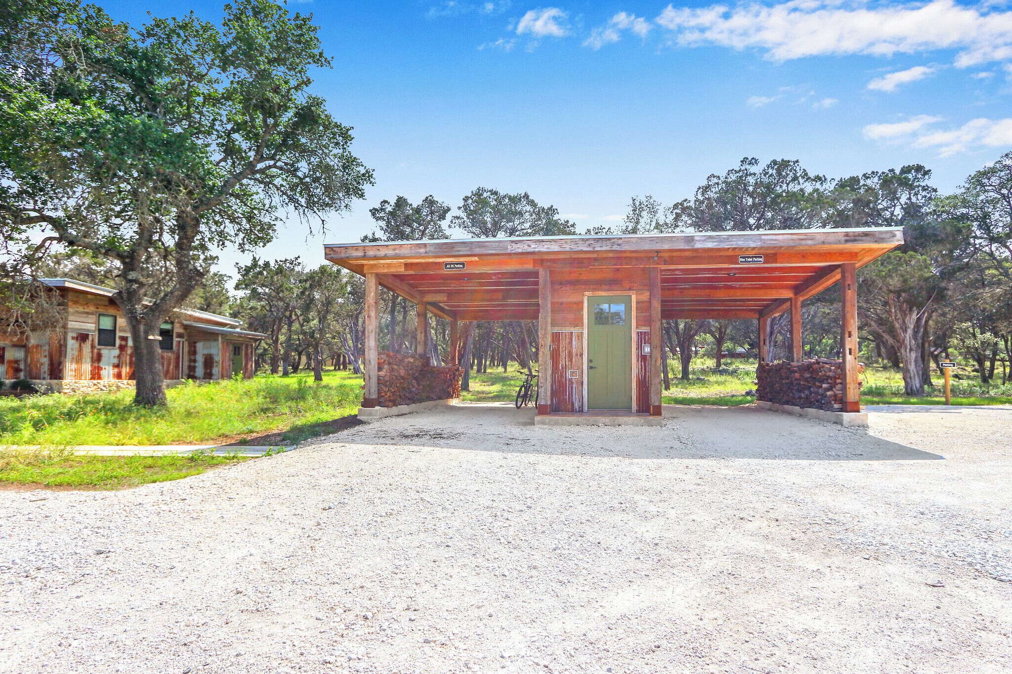 A rustic wooden structure with a covered entrance, surrounded by trees and a gravel path.