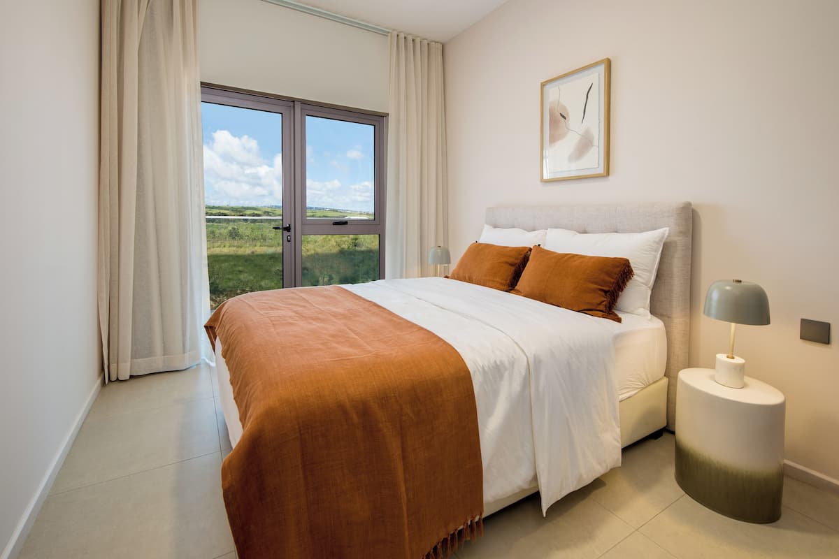 Een slaapkamer met een groot bed, een nachtkastje, een raam met gordijnen en een ingelijste foto aan de muur.