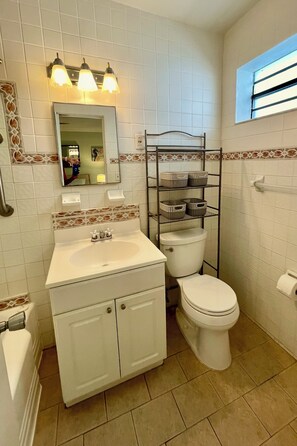 A bathroom with a white sink, mirror, and toilet. There is a shelf with baskets and a window with blinds. - BRAND NEW FOR 4-1/1 BEACH VIEW-HEATED POOL-PARKING (Hollywood)