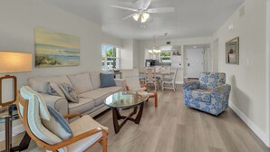 A spacious living room with a sofa, armchairs, a glass coffee table, and a ceiling fan.