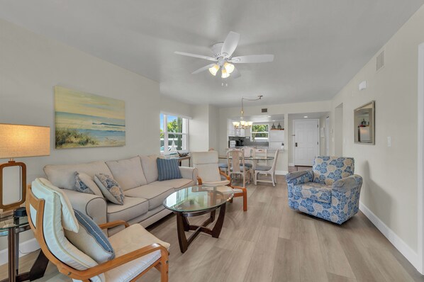 A spacious living room with a sofa, armchairs, a glass coffee table, and a ceiling fan.