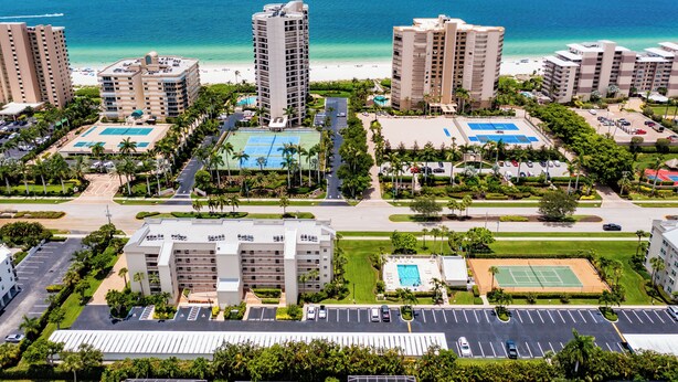 A resort with multiple high-rise buildings, a beach, and various amenities including tennis courts and parking areas.