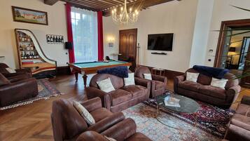 Una sala de estar con sofás de cuero, una mesa de billar, una estantería y un televisor.