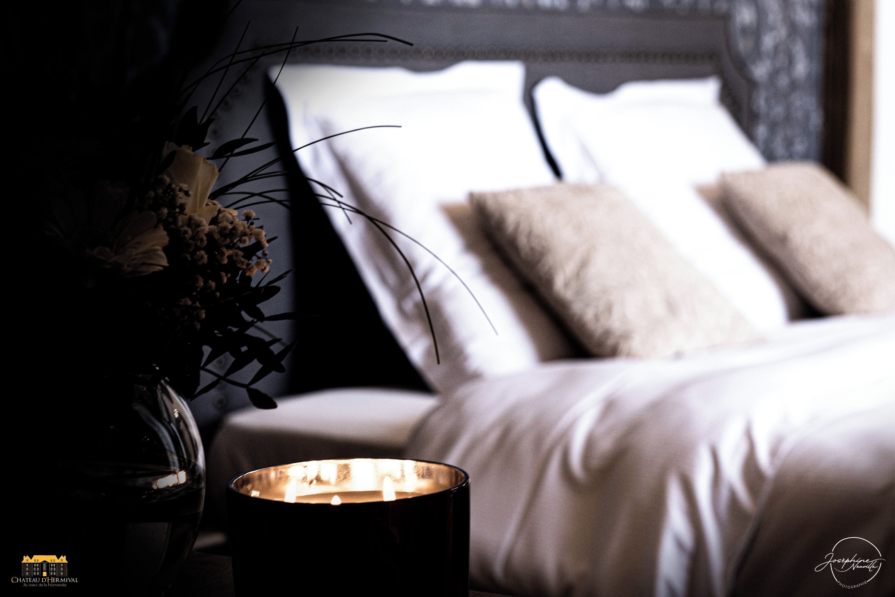 A dimly lit room with a bed, a vase with flowers, and a candle on a table.