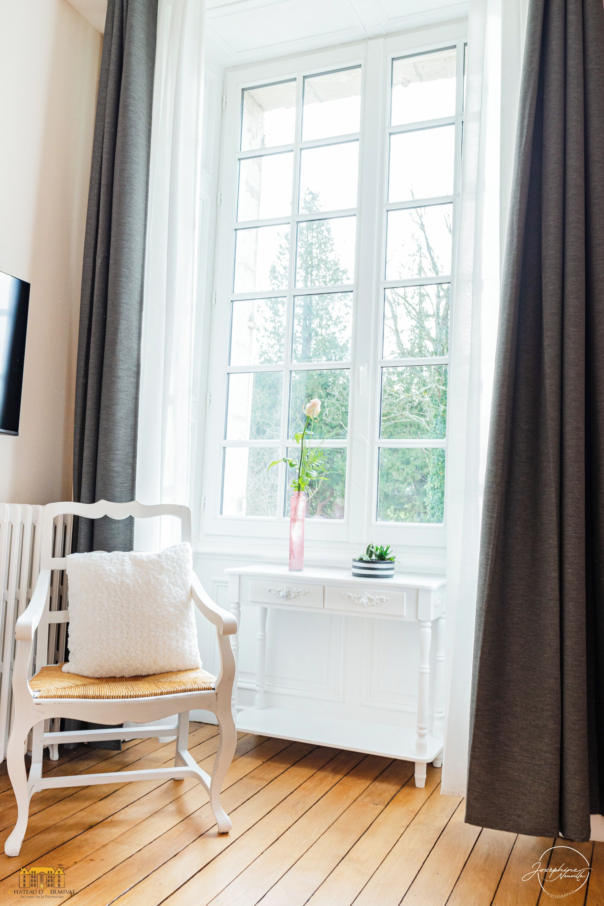 A white chair with a cushion, a white console table, and a window with curtains.