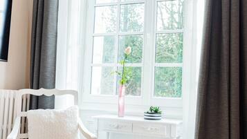 A white chair with a cushion, a white console table, and a window with curtains.