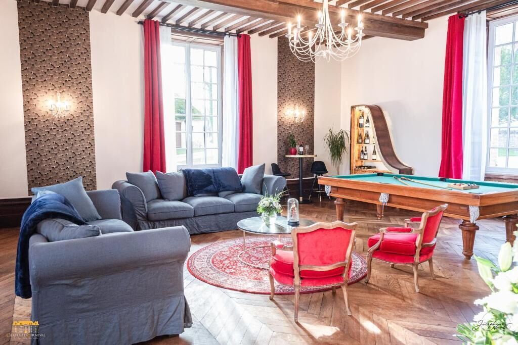 Ein Wohnzimmer mit Billardtisch, roten und grauen Sofas und einem rot-weißen Teppich.