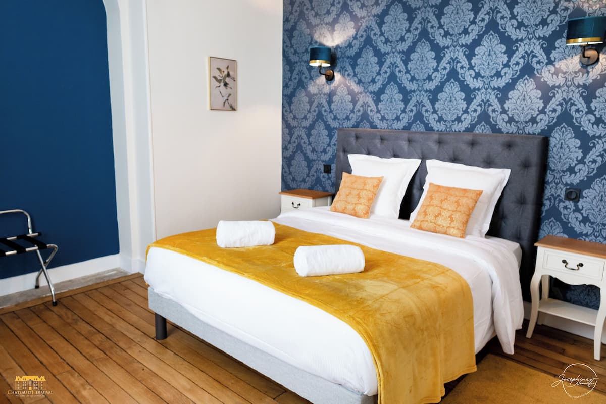 A neatly made bed with a yellow throw blanket and two white towels, a nightstand with a lamp, and a blue patterned wall.