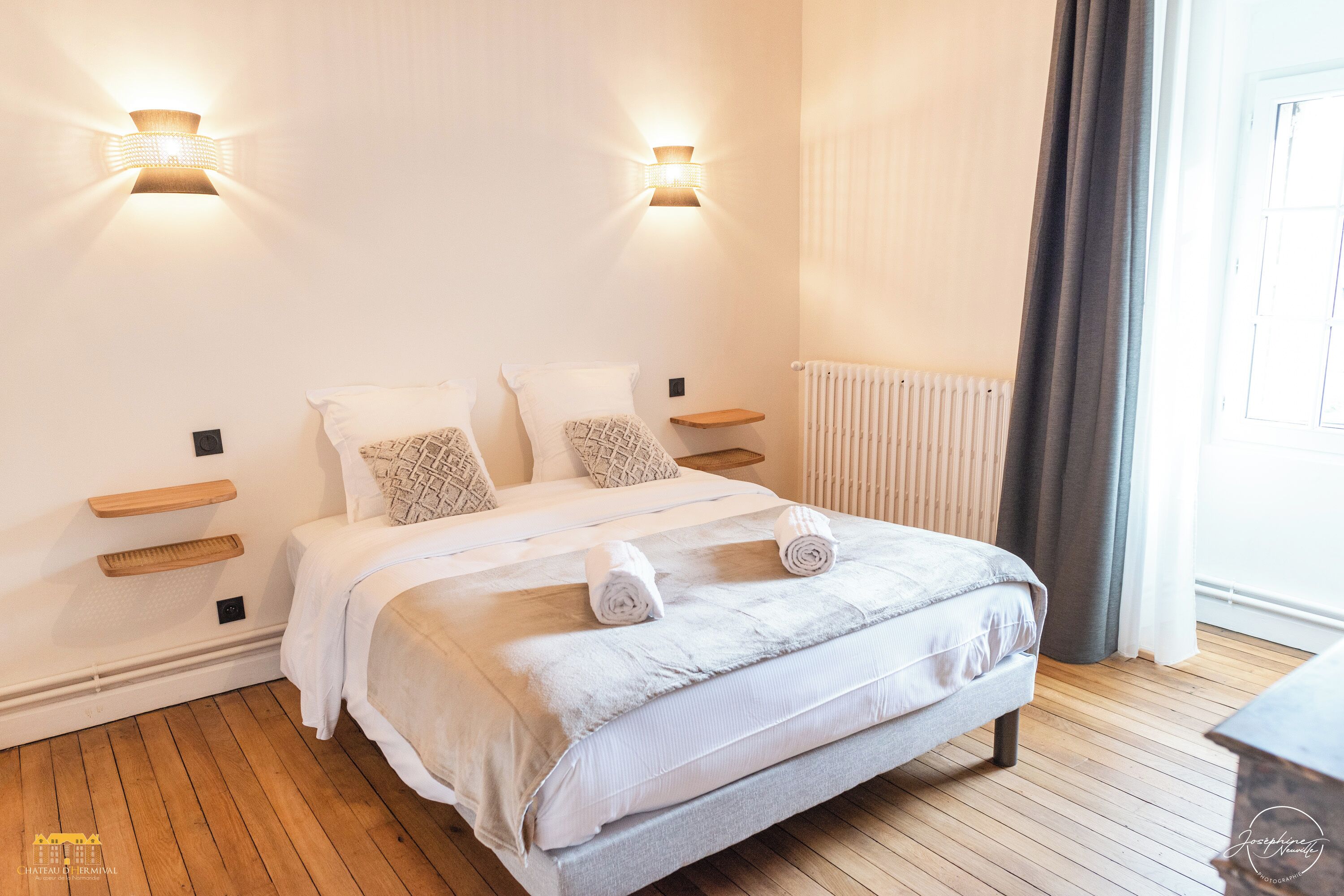 A modern bedroom with a large bed, two wall-mounted light fixtures, a wooden bedside table, and a radiator.