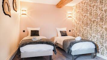 A hotel room with two beds, each with a pillow and a towel, a wooden ceiling beam, and a floral wallpaper on one wall.