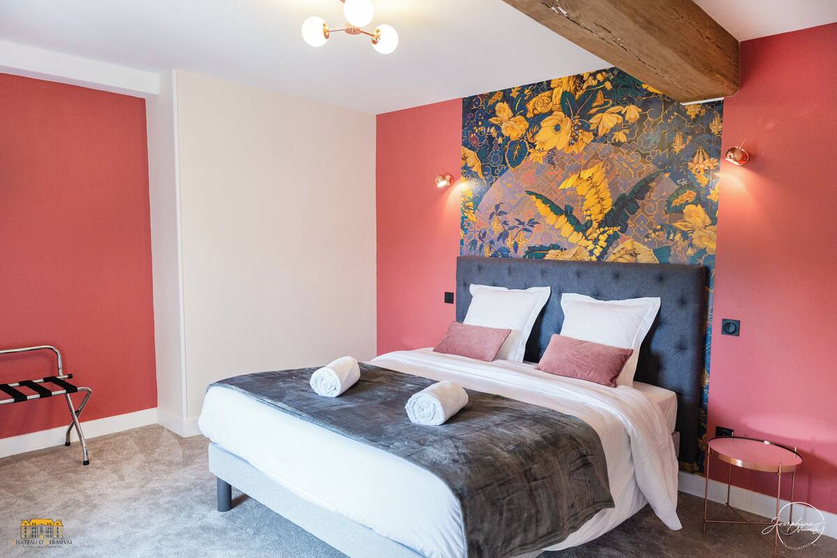A modern bedroom with a large bed, a headboard with a floral mural, a bedside table, and a red accent wall.
