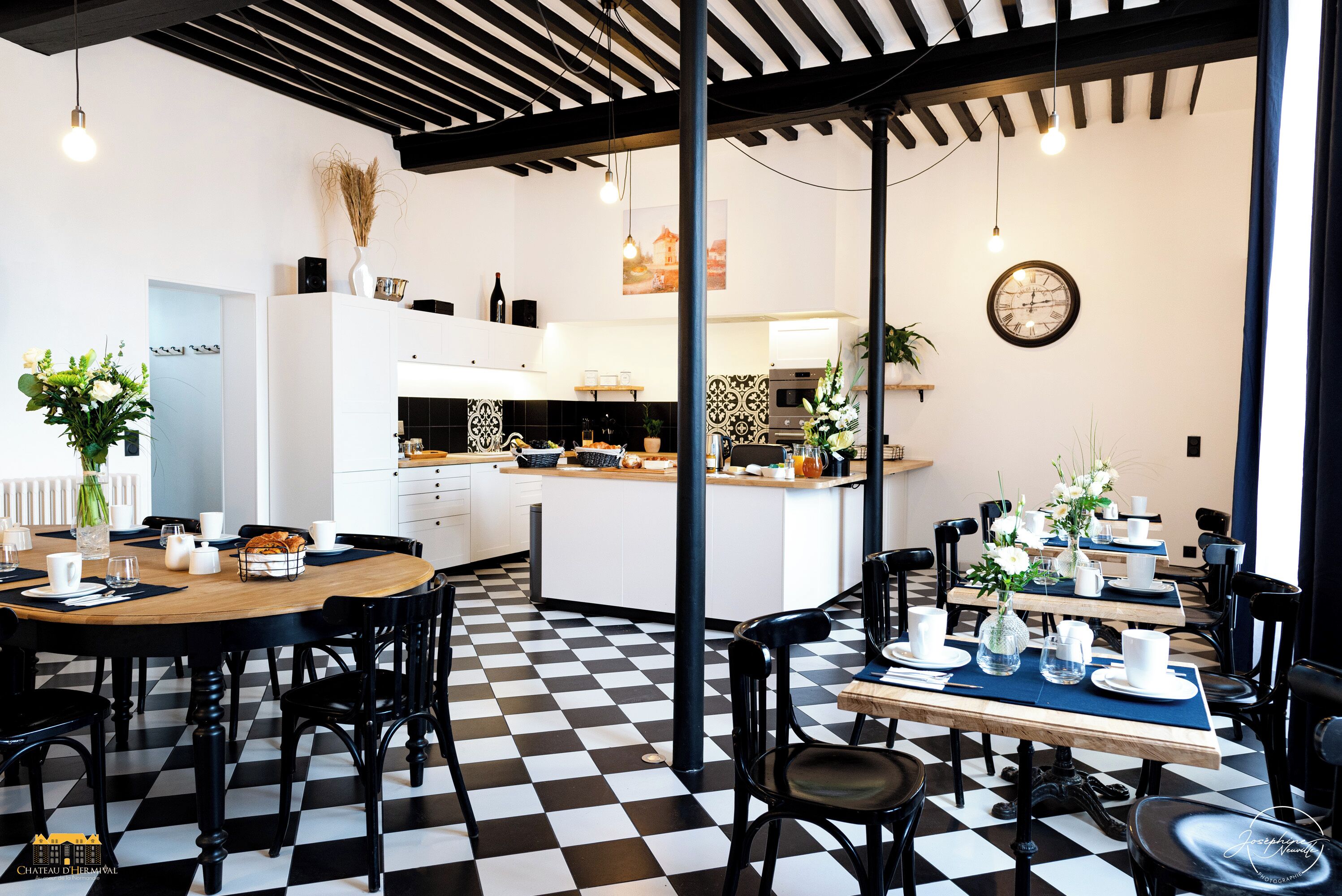 A modern kitchen with a central island, black and white checkered floor, and a dining area with tables set for four.