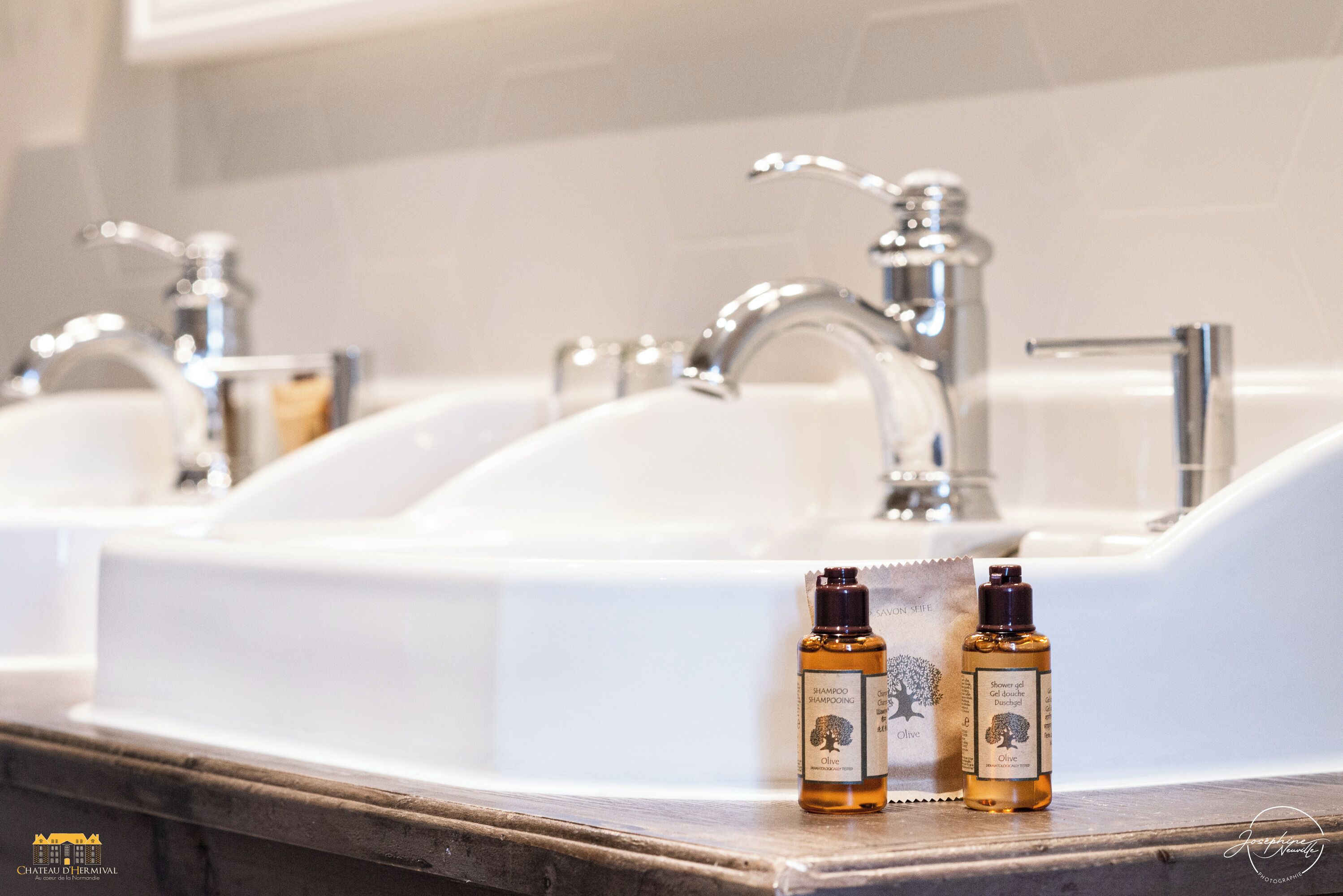 Une salle de bain avec trois lavabos et deux bouteilles d’huile d’olive posées sur le comptoir.