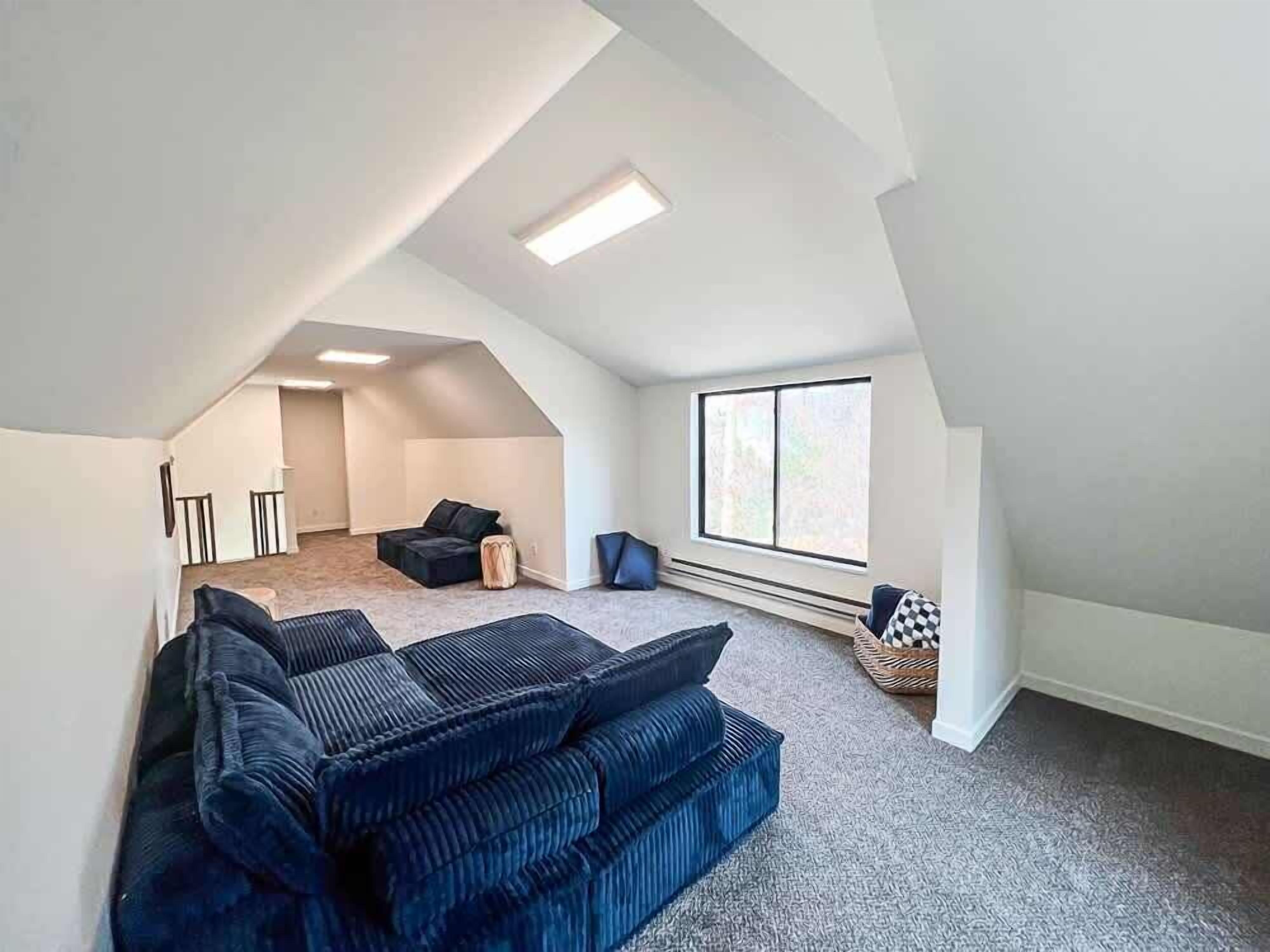 Habitación estilo loft con techo alto, ventana grande, sofá integrado y un pequeño rincón de estar.