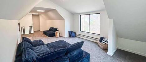 Habitación estilo loft con techo alto, ventana grande, sofá integrado y un pequeño rincón de estar.