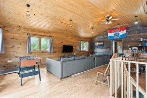 A cozy wooden interior with a sofa, a foosball table, and a flag on the wall. - Hwy 91 Log Cabin — 2BR/2BA, Fireplace, Mtn Views, Sleeps 4 (Leadville)