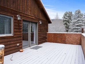 A wooden cabin with a snow-covered deck, a sliding glass door, and a lantern on the exterior wall. - Hwy 91 Log Cabin — 2BR/2BA, Fireplace, Mtn Views, Sleeps 4 (Leadville)