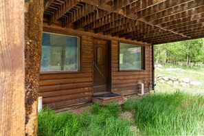 A wooden cabin with a covered porch, a door, and large windows. - Hwy 91 Log Cabin — 2BR/2BA, Fireplace, Mtn Views, Sleeps 4 (Leadville)