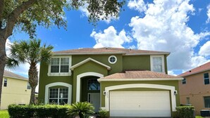 A two-story house with a front garage, a well-maintained lawn, and a palm tree.