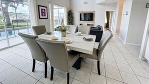 A dining area with a large table, chairs, a TV, and a view of the outdoors.