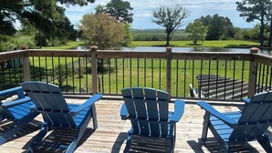 A wooden deck with blue Adirondack chairs overlooking a grassy area with trees and a body of water.