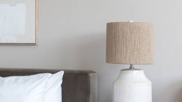 Ein ordentlich bezogenes Bett mit weißer Bettwäsche, ein Nachttisch aus Holz mit Lampe und ein gerahmtes Bild an der Wand.