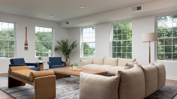 A spacious living room with a large beige sectional sofa, two blue armchairs, a wooden coffee table, and a floor lamp.