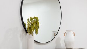 A modern, minimalist console table with a large mirror, a white vase, and a potted plant.