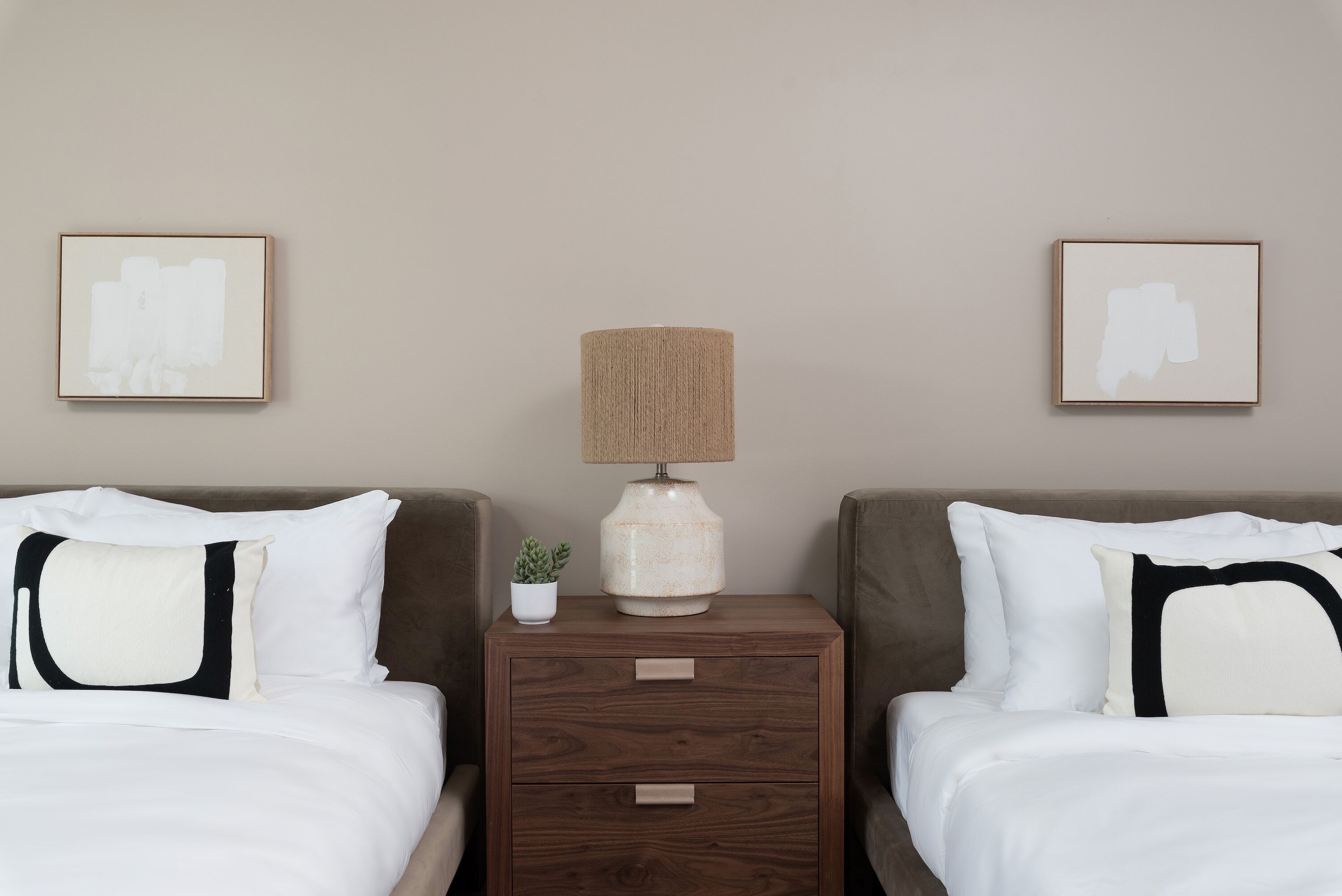 A hotel room with two beds, a nightstand with a lamp, and two framed pictures on the wall.