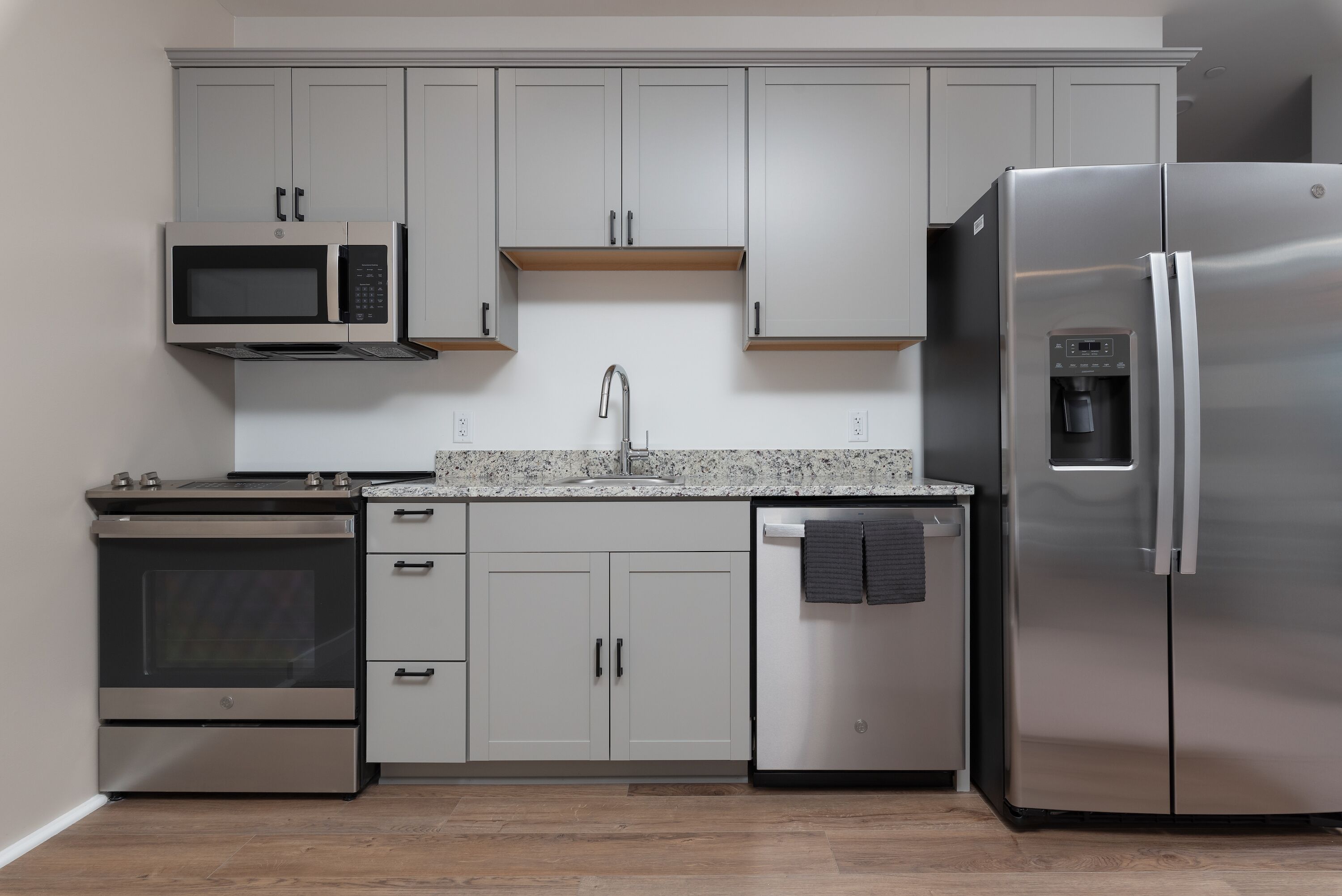 A modern kitchen with stainless steel appliances, grey cabinets, and a granite countertop.
