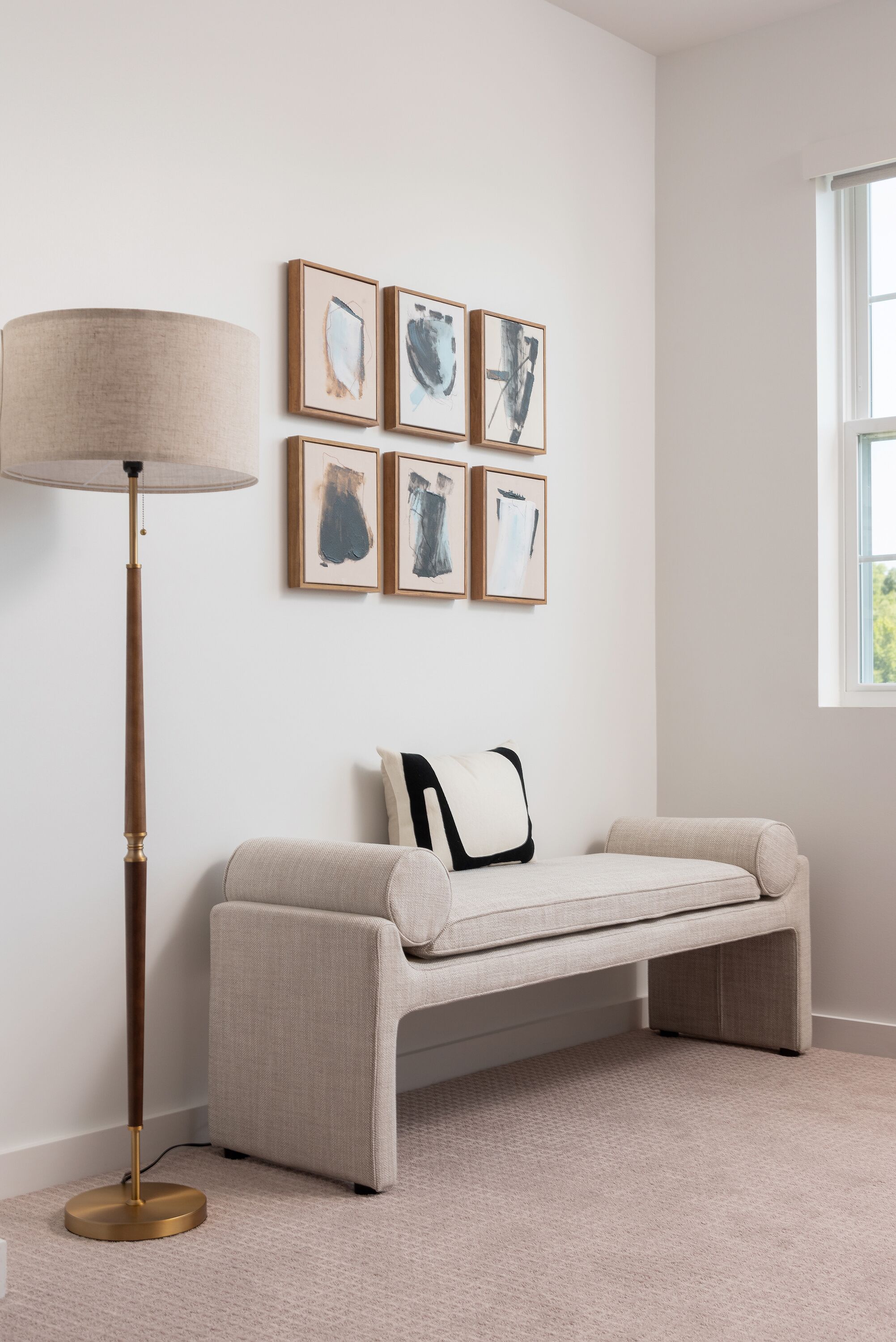 A room with a beige sofa, a floor lamp, and four framed artworks on the wall.